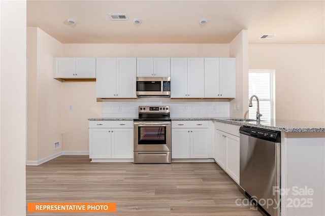 kitchen featuring a peninsula, light wood-style floors, visible vents, appliances with stainless steel finishes, and a sink