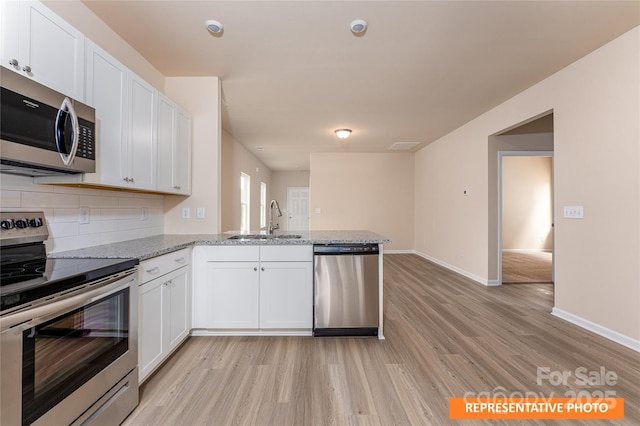 kitchen featuring a peninsula, a sink, stainless steel appliances, light wood finished floors, and decorative backsplash