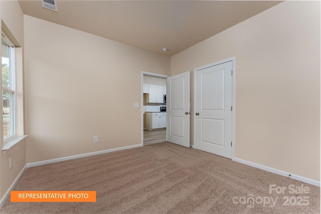 unfurnished bedroom featuring visible vents, light colored carpet, and baseboards