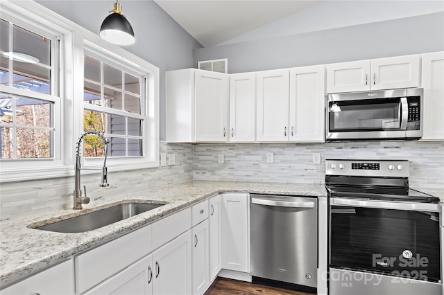 kitchen featuring lofted ceiling, sink, appliances with stainless steel finishes, light stone countertops, and white cabinets