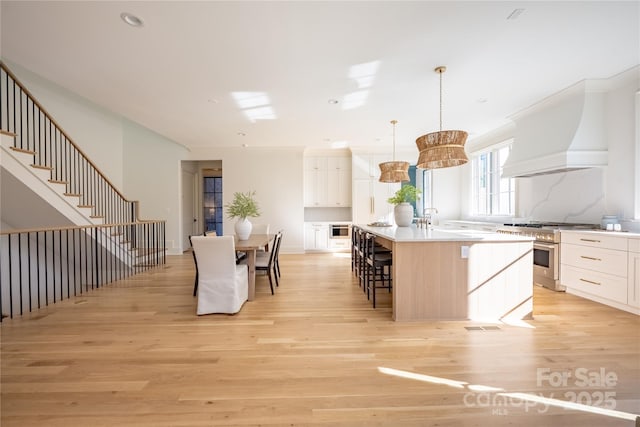 kitchen with premium range hood, decorative light fixtures, tasteful backsplash, an island with sink, and high end stainless steel range