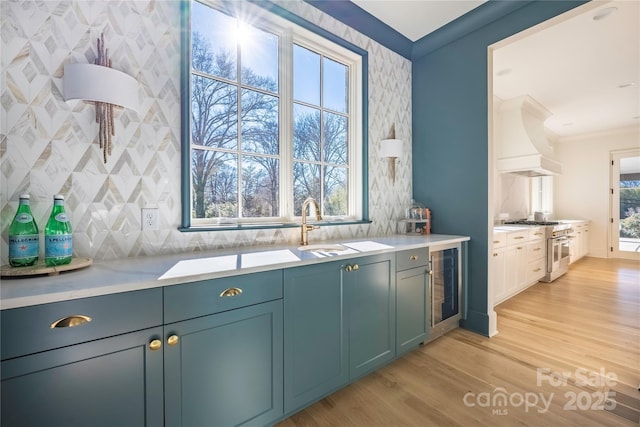 kitchen featuring premium range hood, light hardwood / wood-style flooring, ornamental molding, beverage cooler, and high end stove