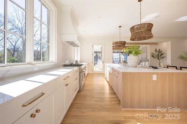 kitchen with premium range hood, pendant lighting, high end stove, sink, and white cabinets