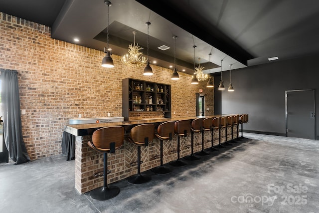 bar featuring a raised ceiling, brick wall, pendant lighting, and concrete floors