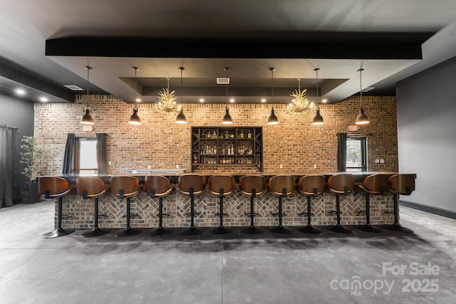 bar with a tray ceiling, hanging light fixtures, and concrete floors