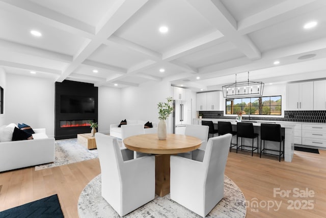 dining space with an inviting chandelier, a fireplace, light wood-type flooring, coffered ceiling, and beam ceiling