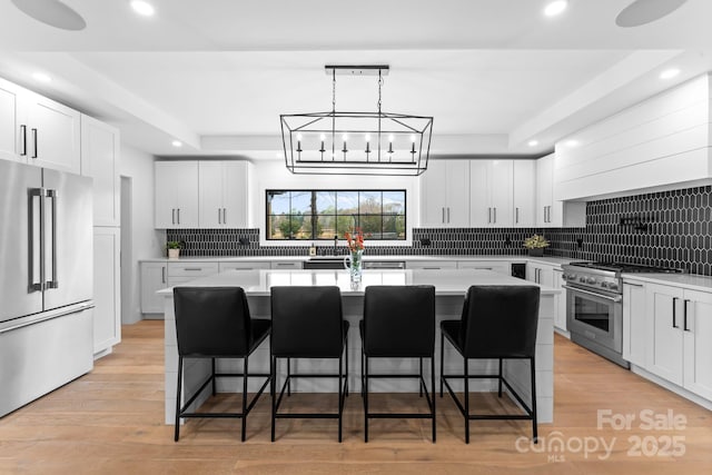 kitchen featuring white cabinetry, premium appliances, a breakfast bar area, and a center island with sink