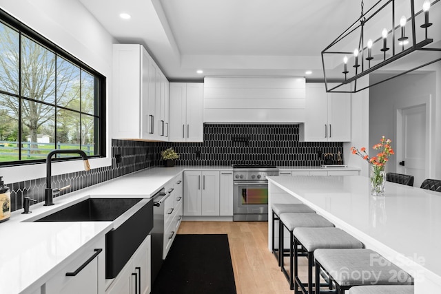 kitchen featuring light hardwood / wood-style flooring, high end range, a kitchen breakfast bar, white cabinets, and decorative light fixtures