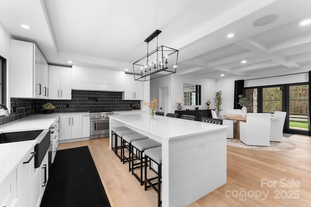 kitchen featuring sink, a breakfast bar area, white cabinetry, a center island, and stainless steel range