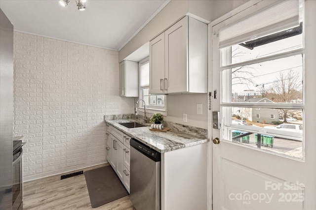 kitchen with appliances with stainless steel finishes, white cabinetry, sink, light stone countertops, and light wood-type flooring