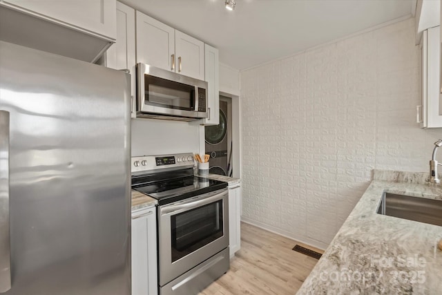 kitchen with stacked washing maching and dryer, brick wall, white cabinetry, sink, and stainless steel appliances