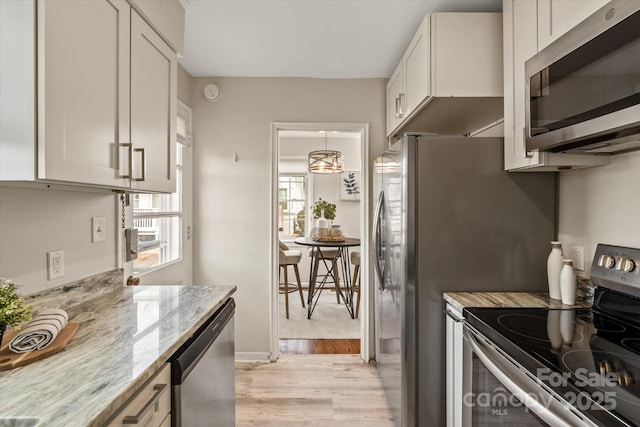 kitchen with light stone counters, light hardwood / wood-style flooring, white cabinets, and appliances with stainless steel finishes