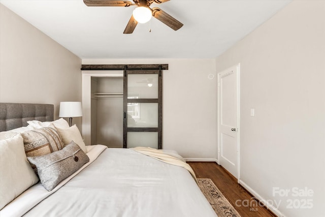 bedroom with a barn door, dark hardwood / wood-style floors, ceiling fan, and a closet