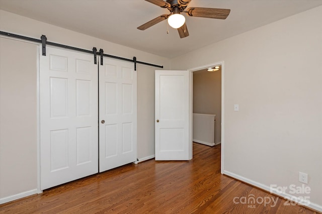 unfurnished bedroom with a barn door, hardwood / wood-style floors, ceiling fan, and a closet