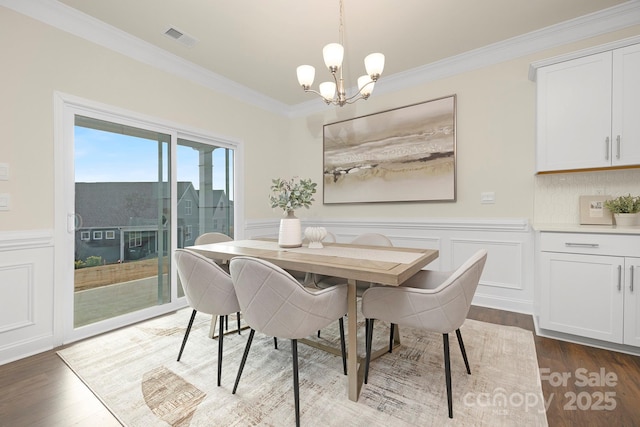 dining space with dark wood-type flooring, ornamental molding, and a notable chandelier