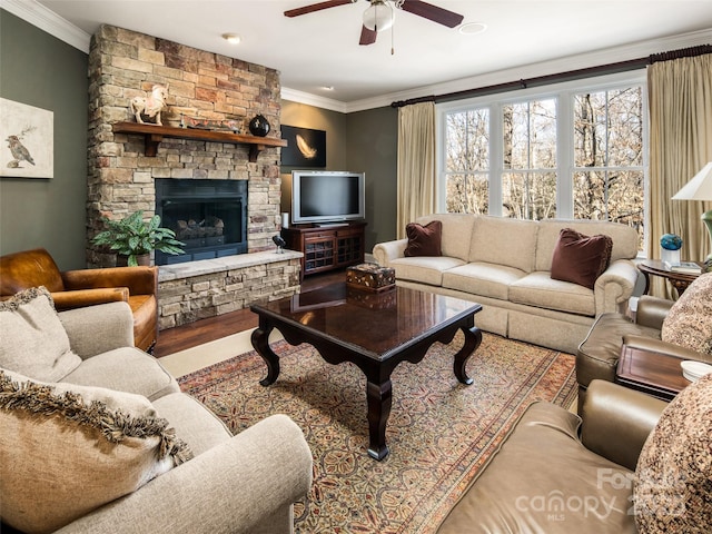 living room with ceiling fan, crown molding, hardwood / wood-style flooring, and a stone fireplace