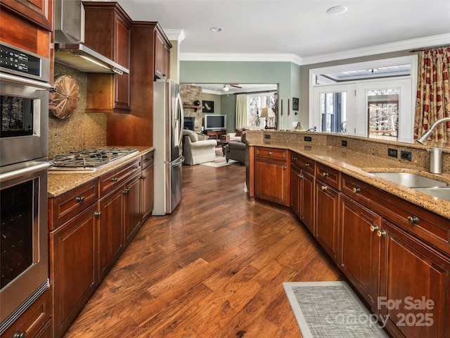 kitchen with stainless steel appliances, decorative backsplash, wall chimney range hood, light stone countertops, and sink