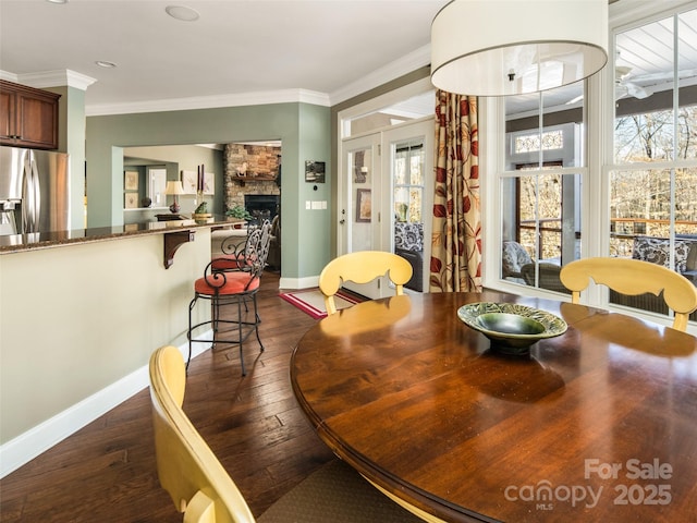 dining space featuring dark wood-type flooring, ornamental molding, and a fireplace