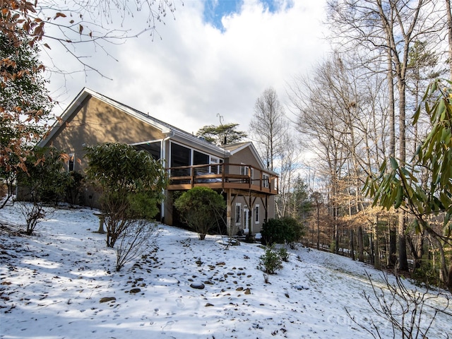 snow covered back of property featuring a deck and a sunroom