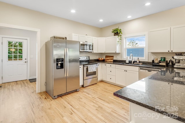 kitchen featuring sink, white cabinetry, dark stone countertops, stainless steel appliances, and light hardwood / wood-style floors