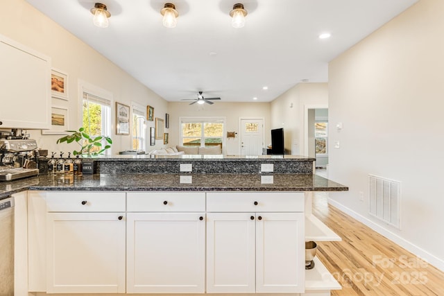 kitchen with white cabinetry, light hardwood / wood-style floors, dark stone counters, and a healthy amount of sunlight