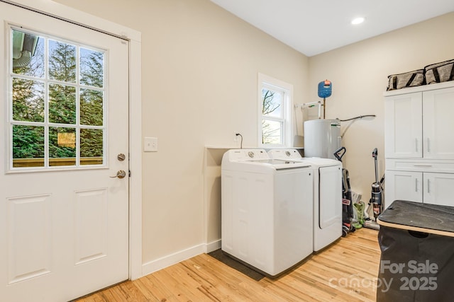 washroom featuring water heater, light hardwood / wood-style flooring, cabinets, and washing machine and clothes dryer