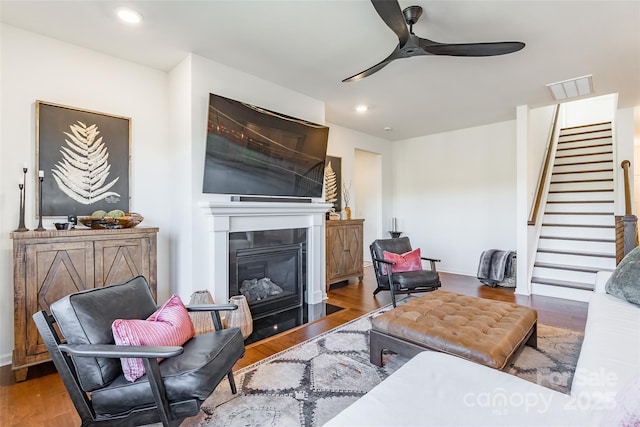 living area with wood finished floors, visible vents, a ceiling fan, stairs, and a glass covered fireplace