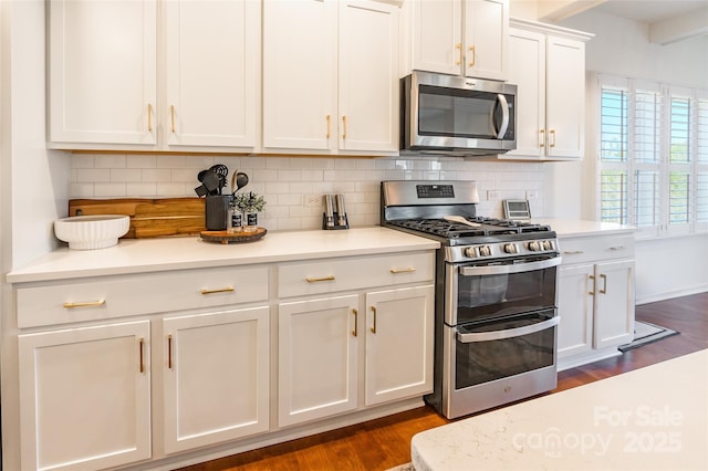 kitchen with light stone counters, dark wood-type flooring, white cabinets, appliances with stainless steel finishes, and tasteful backsplash