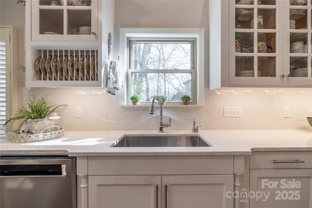 kitchen featuring white cabinetry, tasteful backsplash, stainless steel dishwasher, light stone counters, and sink