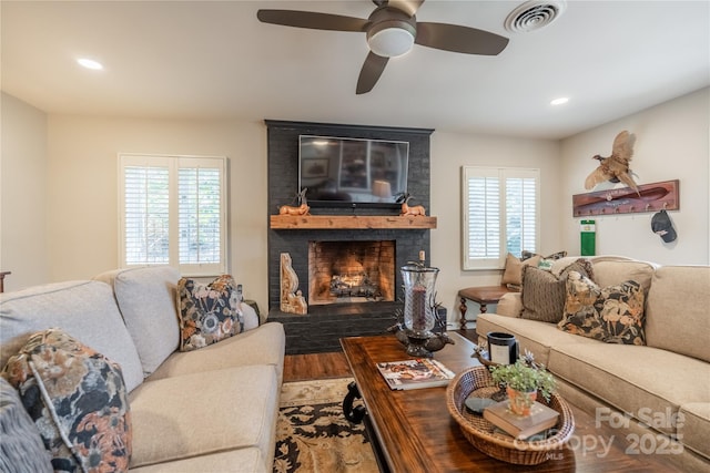 living room with ceiling fan, a healthy amount of sunlight, a brick fireplace, and hardwood / wood-style floors