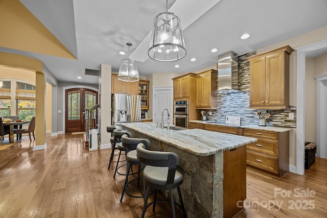 kitchen featuring decorative light fixtures, a kitchen island with sink, wall chimney exhaust hood, and stainless steel appliances