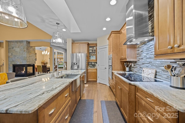 kitchen with a stone fireplace, a large island, backsplash, decorative light fixtures, and wall chimney exhaust hood