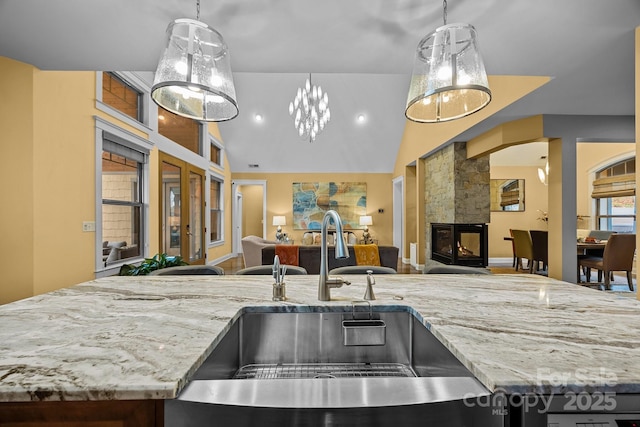 kitchen with decorative light fixtures, lofted ceiling, a fireplace, light stone countertops, and sink