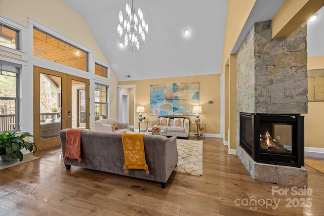 living room featuring an inviting chandelier, hardwood / wood-style flooring, a stone fireplace, high vaulted ceiling, and french doors