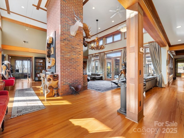 entryway featuring crown molding, wood-type flooring, ceiling fan with notable chandelier, and a high ceiling