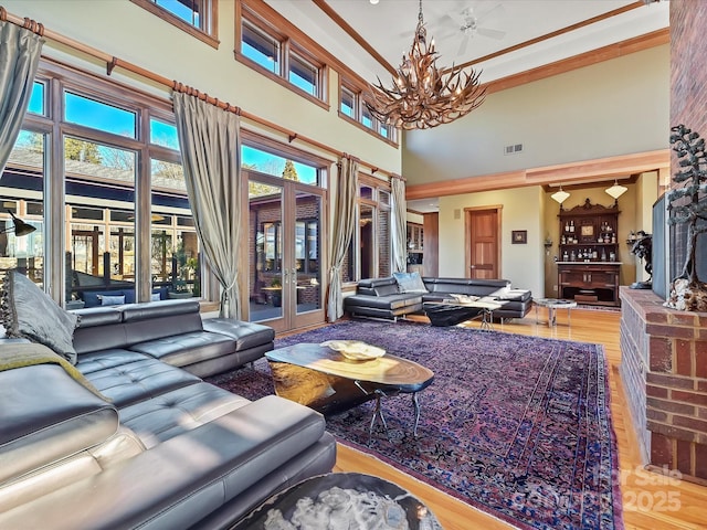 living room with an inviting chandelier, a high ceiling, light hardwood / wood-style floors, a brick fireplace, and french doors