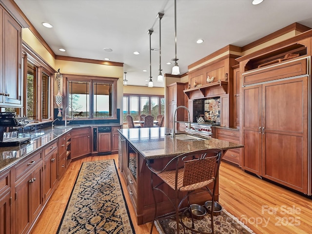 kitchen featuring a kitchen bar, sink, hanging light fixtures, dark stone countertops, and an island with sink