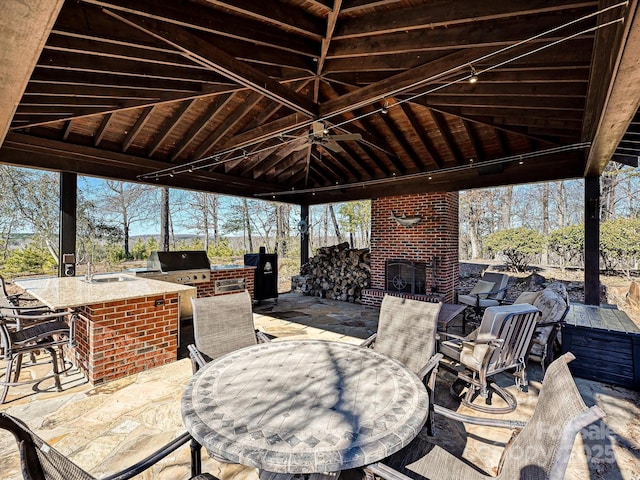 view of patio with an outdoor kitchen, an outdoor wet bar, ceiling fan, an outdoor brick fireplace, and a gazebo