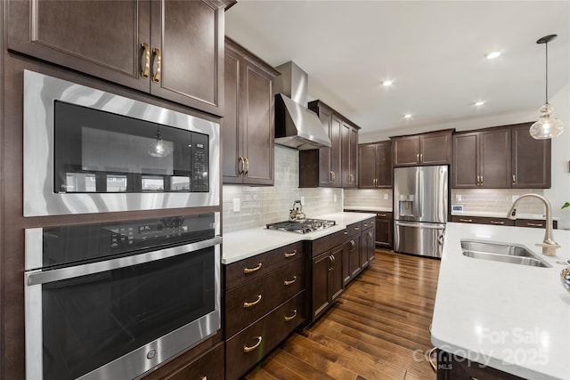 kitchen with sink, wall chimney range hood, appliances with stainless steel finishes, dark brown cabinets, and decorative light fixtures