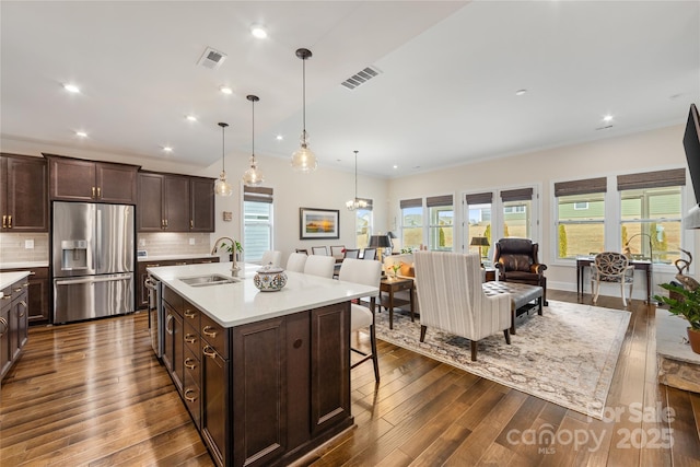 kitchen with sink, a breakfast bar area, stainless steel fridge with ice dispenser, an island with sink, and pendant lighting