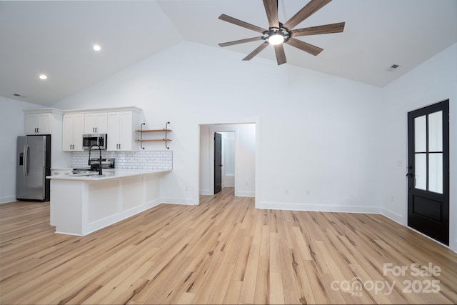 kitchen with high vaulted ceiling, kitchen peninsula, stainless steel appliances, light hardwood / wood-style floors, and white cabinets