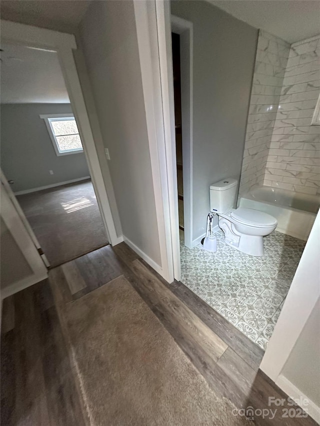 bathroom with hardwood / wood-style flooring, tiled shower / bath, and toilet