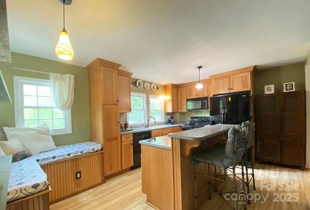 kitchen featuring pendant lighting, a breakfast bar, light hardwood / wood-style floors, and black appliances