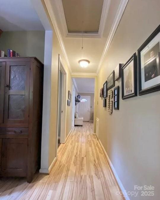 hall with a tray ceiling, ornamental molding, and light wood-type flooring