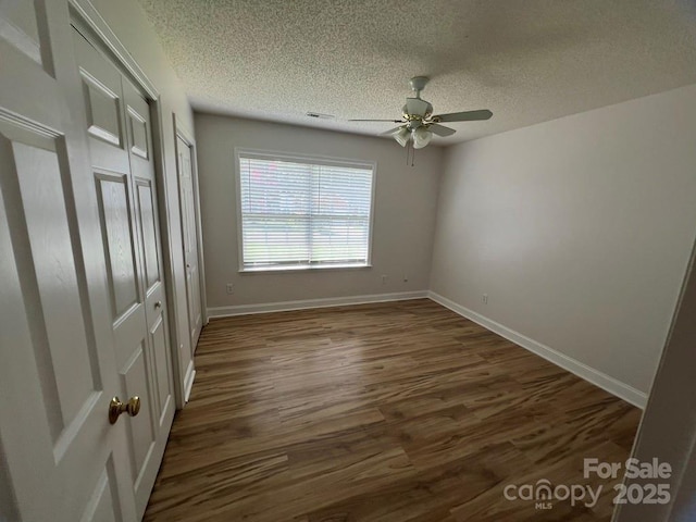 unfurnished bedroom with dark hardwood / wood-style flooring, ceiling fan, a textured ceiling, and multiple closets