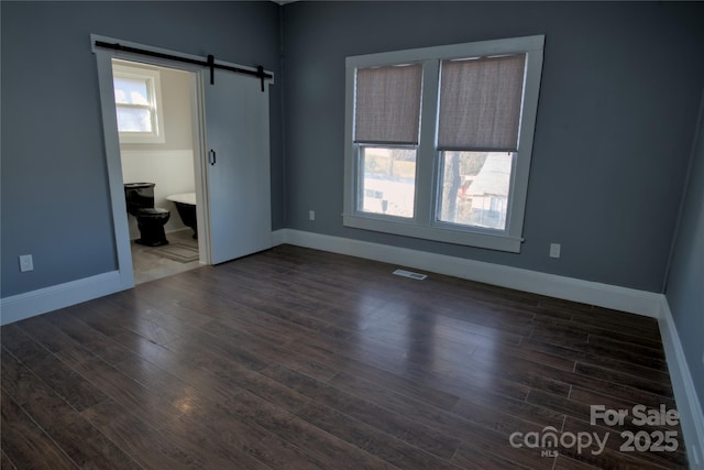 unfurnished bedroom with dark wood-type flooring, ensuite bath, and a barn door