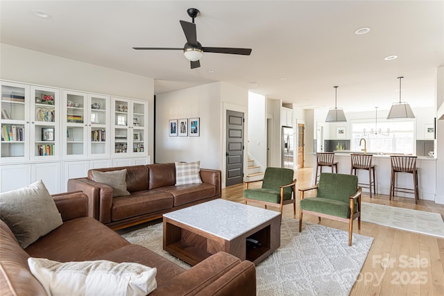 living room featuring ceiling fan with notable chandelier and light wood-type flooring