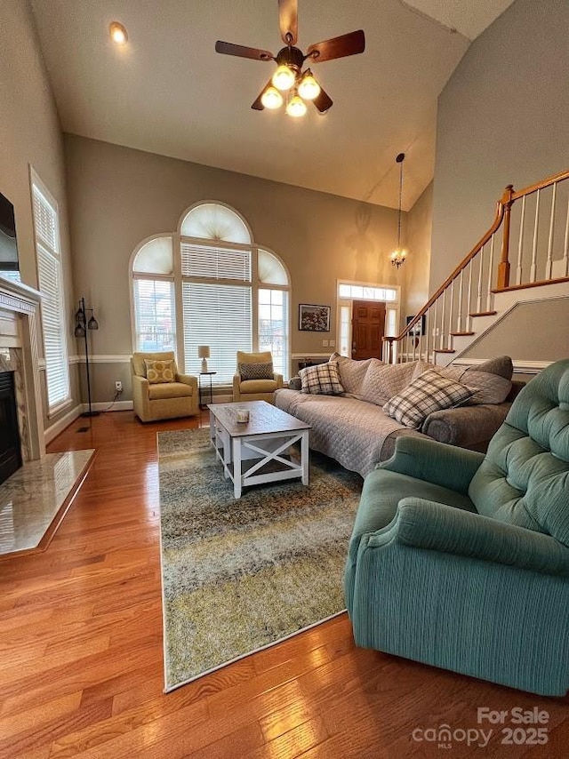 living room with ceiling fan, wood-type flooring, a high end fireplace, and high vaulted ceiling