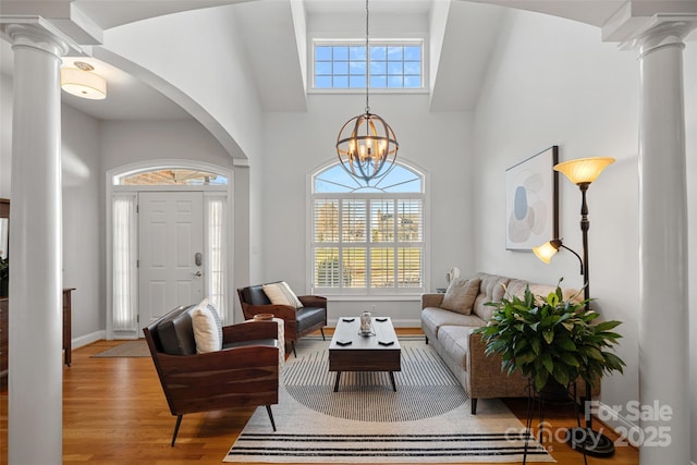 living room with decorative columns, light hardwood / wood-style floors, a high ceiling, and an inviting chandelier