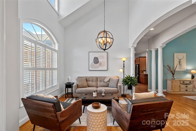 living room with light wood-type flooring, ornate columns, a towering ceiling, and plenty of natural light